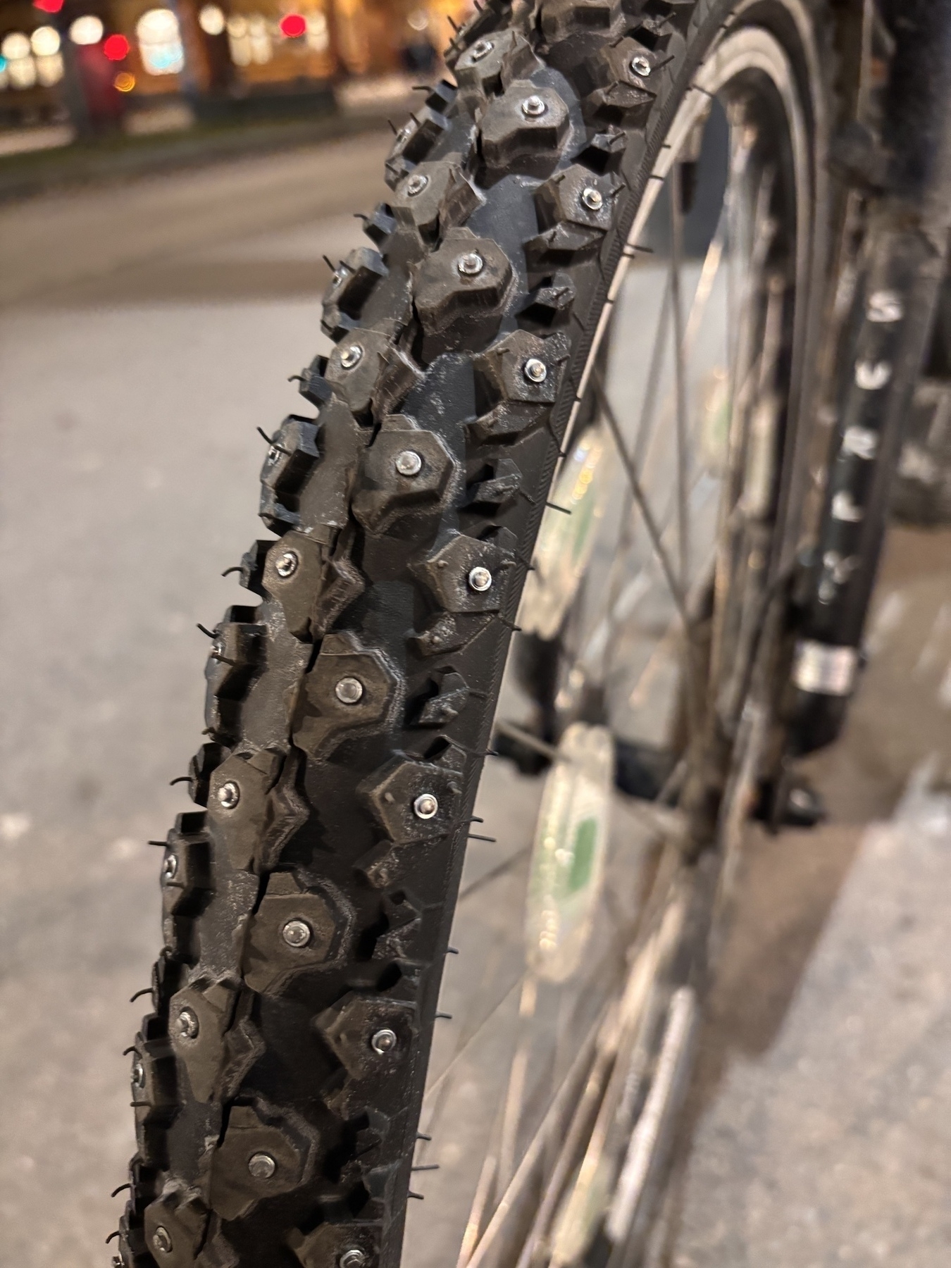 A close-up view of a bicycle tire equipped with metal spikes for enhanced traction during winter 