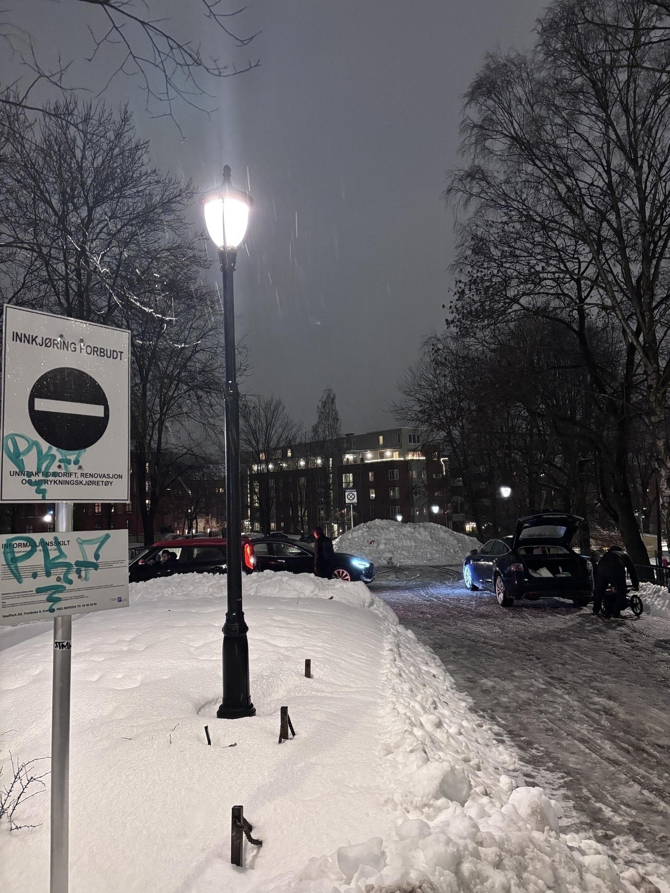 A snowy street scene at night features parked cars, a "No Entry" sign, and buildings in the background.