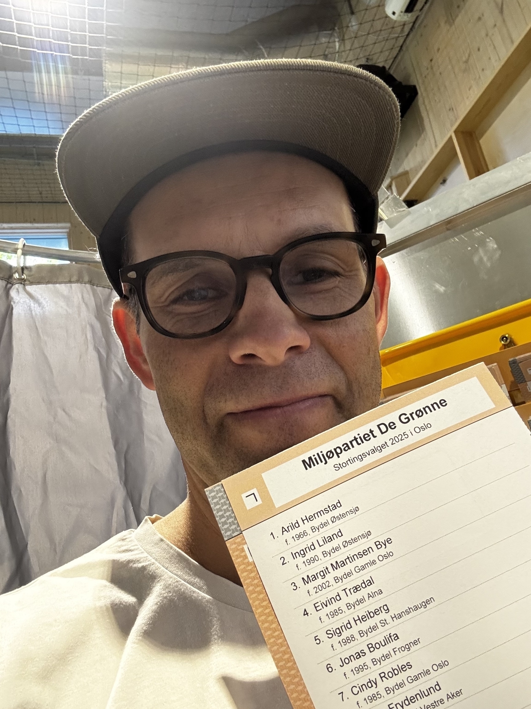 En person med briller og caps (meg) holder en stemmeseddel for Miljøpartiet De Grønne.