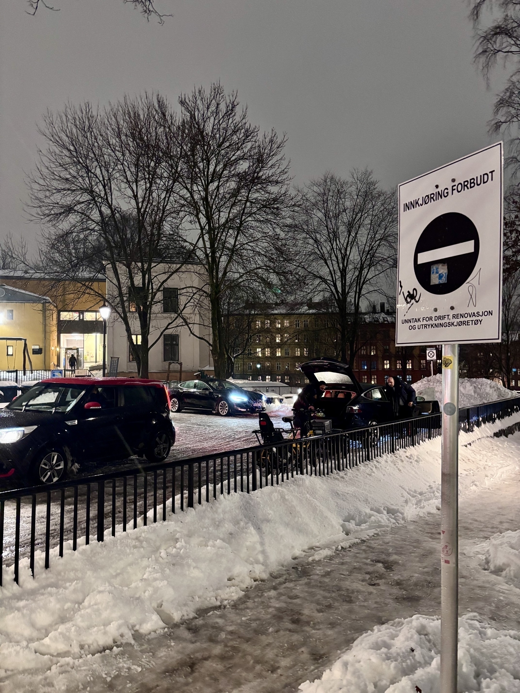 A snowy street scene at night features parked cars, a "No Entry" sign, and buildings in the background.