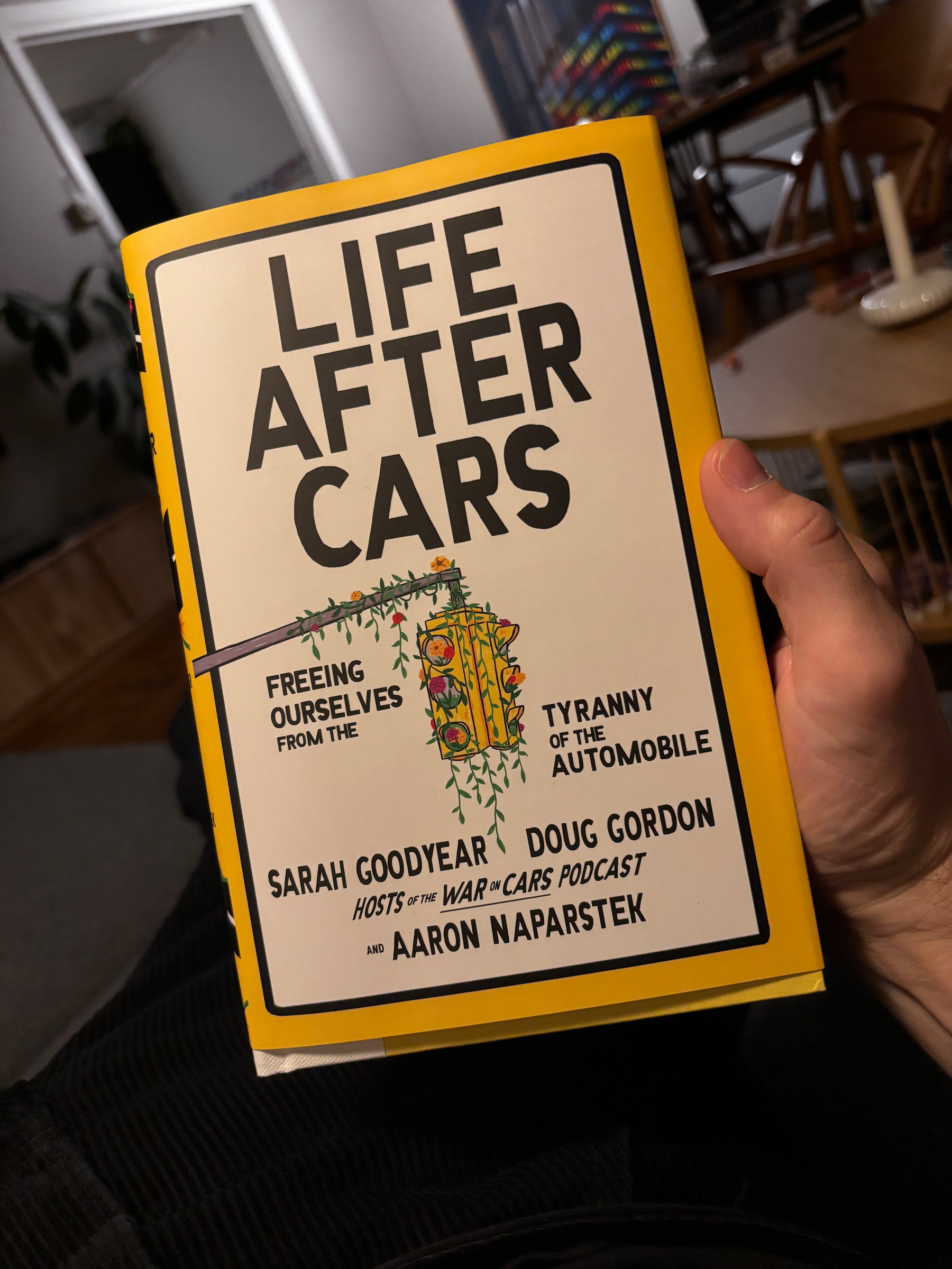 En person holder en bok med gul forside som har tittelen Life After Cars: Freeing Ourselves from the Tyranny of the Automobile.
