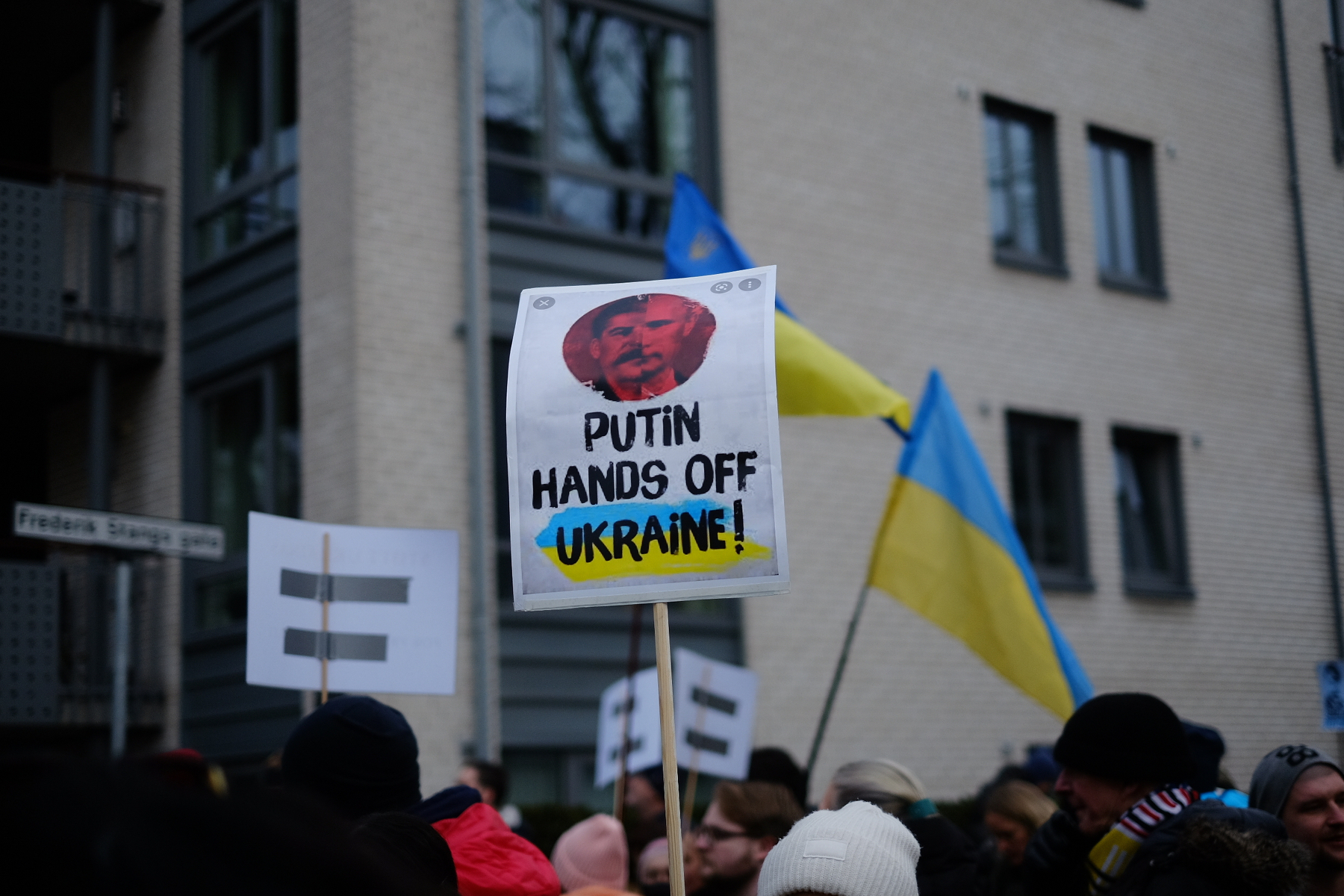 Et folkemøte med en plakat som sier Putin hands off Ukraine! og to ukrainske flagg i bakgrunnen.&10;&10;Oslo, 26. feb. 2022