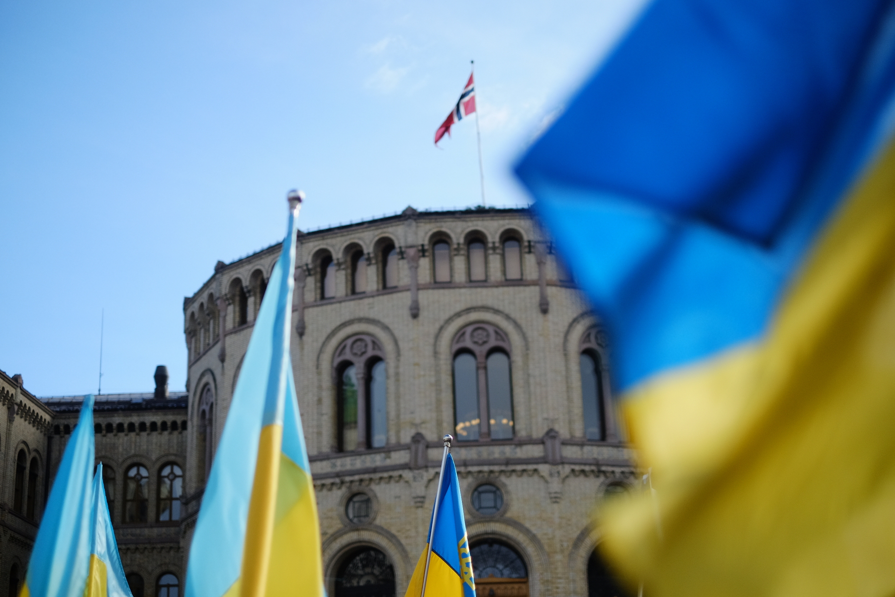 Flere ukrainske flagg vaier foran Stortinget i Norge under en klar himmel.&10;&10;Oslo, 26. feb. 2022